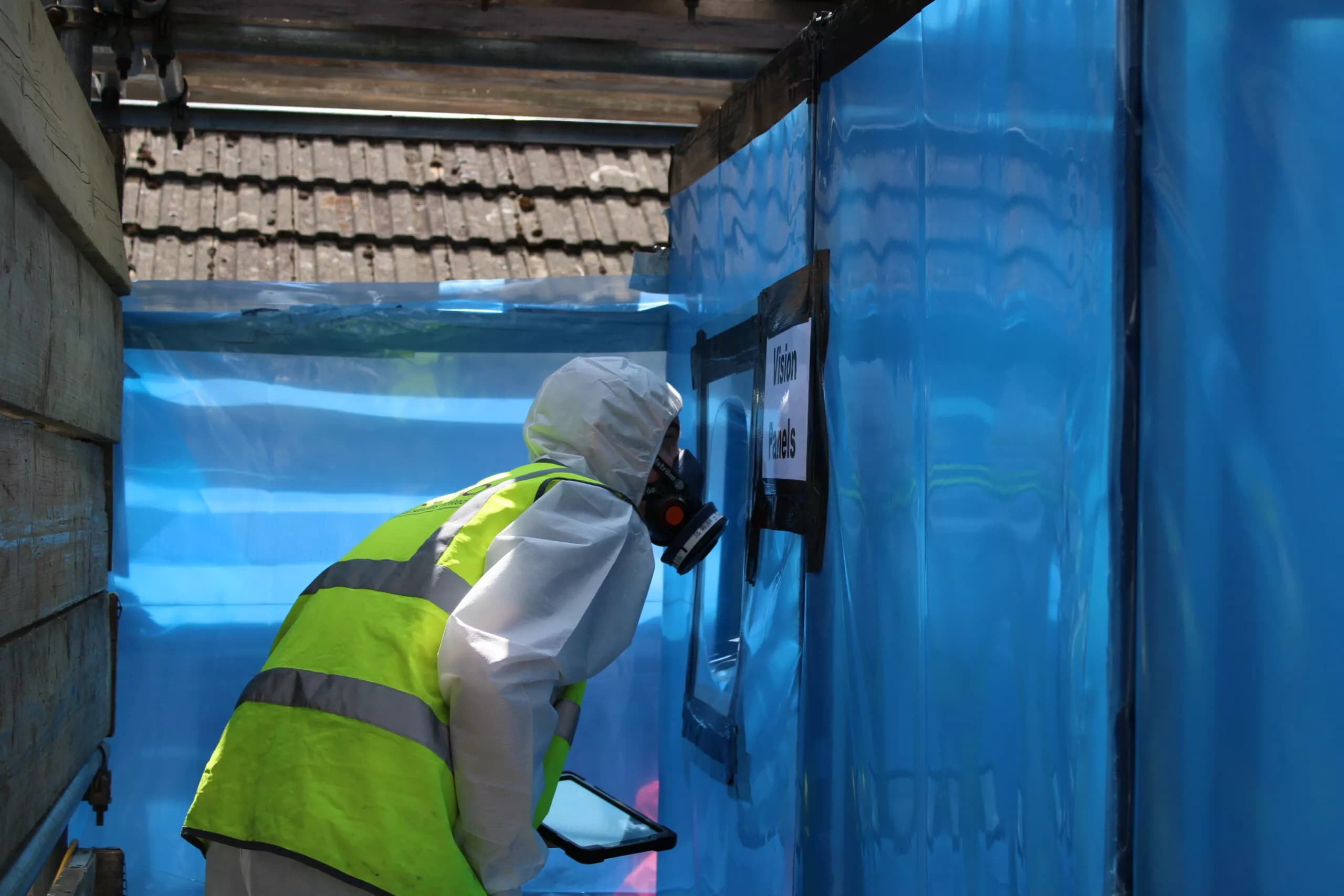 Licensed Surrey Asbestos operative in full PPE inspecting a sealed negative pressure enclosure before licensed asbestos removal in Surrey