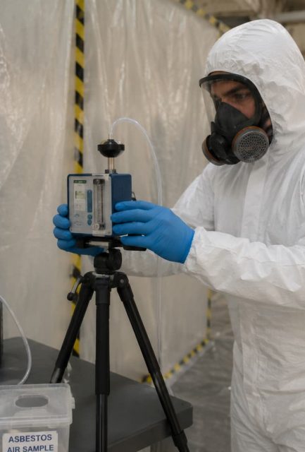 UKAS-accredited analyst operating air monitoring equipment inside a sealed asbestos enclosure during 4-stage clearance testing in Surrey