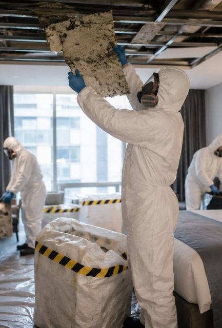 UKATA-trained operatives in full PPE removing asbestos ceiling tiles from a residential property in Surrey with containment sheeting in place