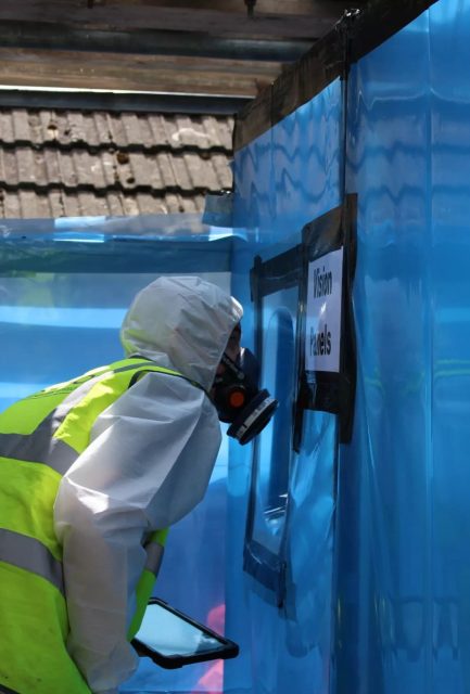 Licensed Surrey Asbestos operative in full PPE inspecting a sealed negative pressure enclosure before licensed asbestos removal in Surrey