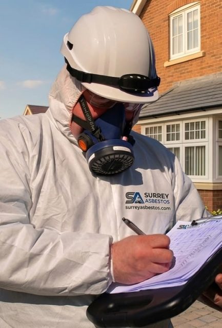 Surrey Asbestos operative in full PPE completing survey documentation outside a Surrey residential property